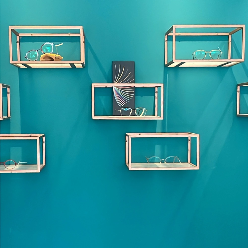 חנות משקפיים עם מסגרות עדינות על קירות בצבע טורקיז, מציעה מגוון משקפי ראייה.
